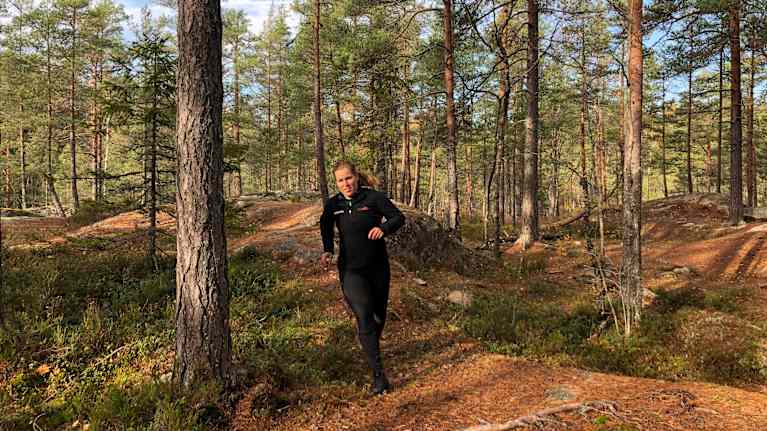 En kvinna som springer i en skog.