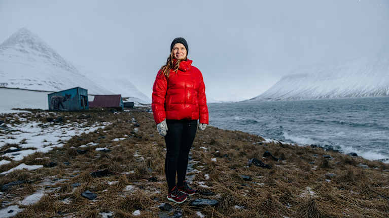 Punaiseen untuvatakkiin pukeutunut henkilö talvisessa maisemassa Ísafjörðurin kylässä Islannissa.