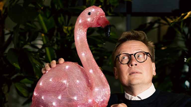 Mikko-Pekka Hanski katsoo flamingon muotoista vaaleanpunaista valaisinta.
