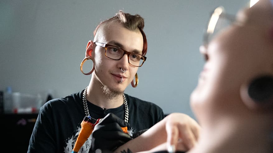 Nuori mies tatuoi tatuointikoneella.