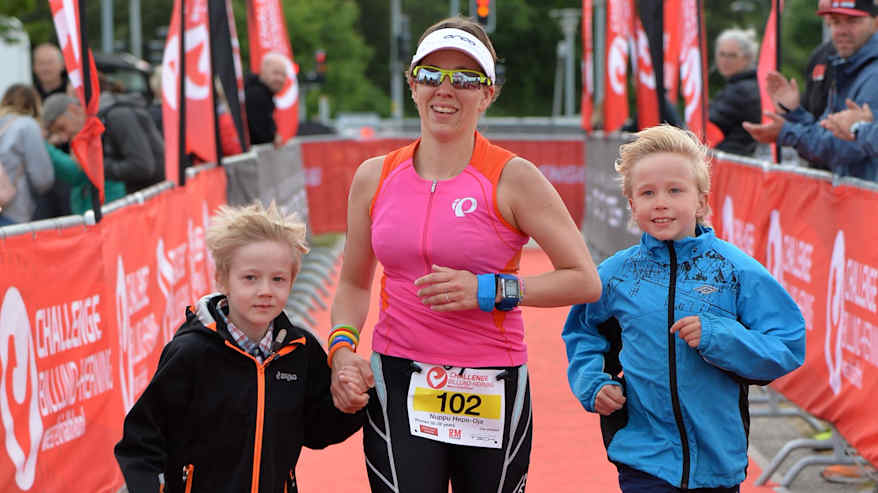 Triathlon-urheilija Nuppu Hepo-oja juoksee kohti maalia triathlon-kilpailussa Tanskassa kahden lapsensa kanssa.