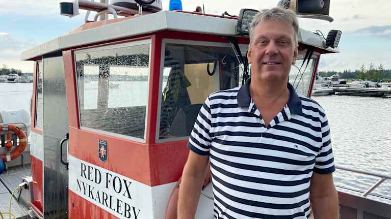 En man står på en räddningsbåt i en hamn.
