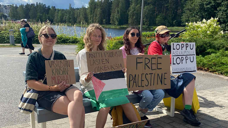 Neljä naista istuu penkillä free palestine-kylttien kanssa.