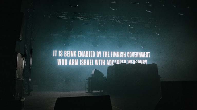 Lavalle on heijastettu teksti: "IT IS BEING ENABLED BY FINNIFH GOVERNMENT WHO ARM ISRAEL WITH ADVANCED WEAPONRY".