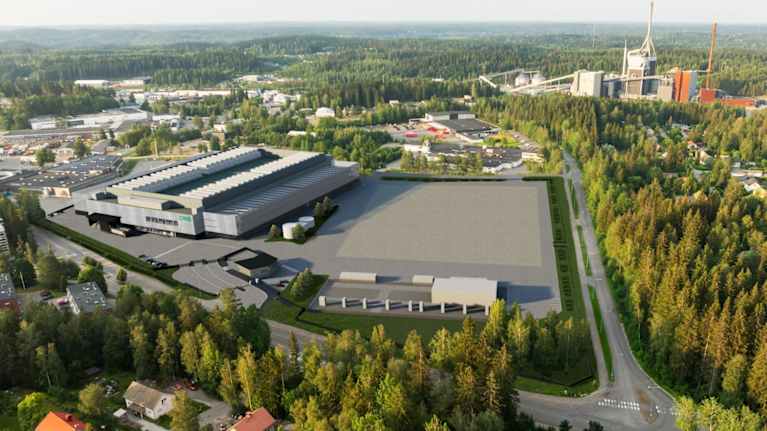 Havainnekuvassa näkyy harmaa iso rakennus ja laaja avoin alue keskellä puista, teitä ja rakennuksia. Taustalla näkyy tehdasrakennelma.