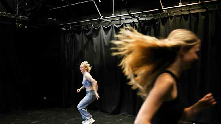 Kaksi henkilöä liikkuu teatterin harjoitustilassa.