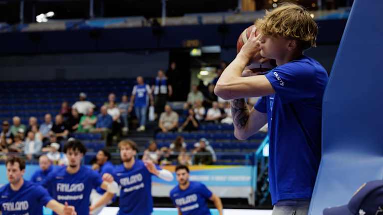 Miikka Muurinen pallon kanssa. Muu joukkue lämmittelee kentällä.