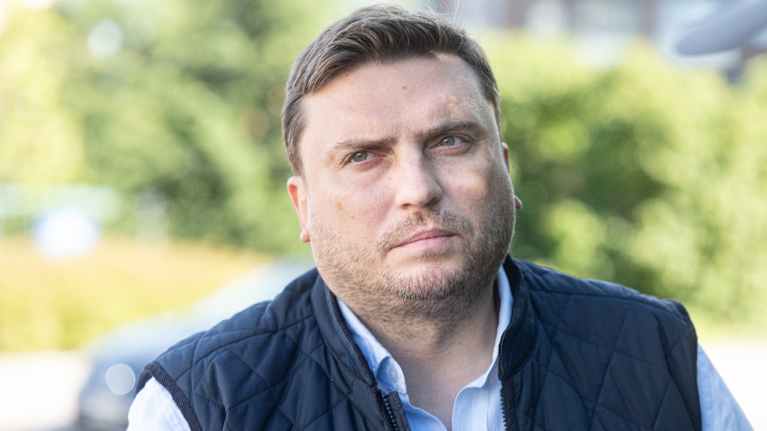 Mies arkisissa vaatteissa katsoo viistosti kohti kameraa.