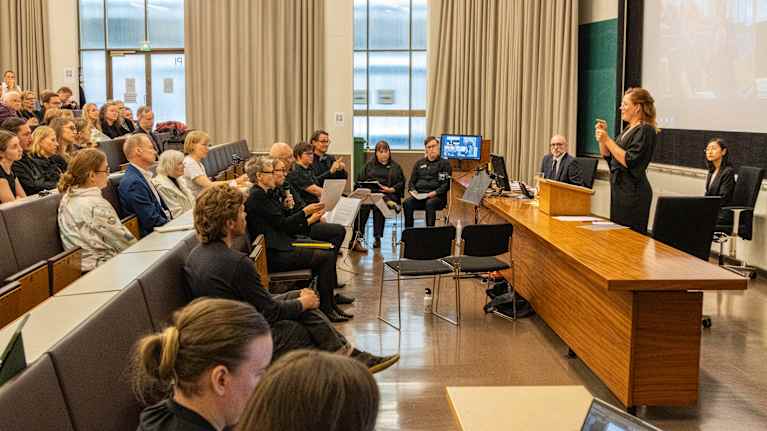 Väittelijä Maija Koivisto kertoo väitöskirjastaan yleisölle. Takana tulkkeja ja opponoija professori Joseph Murray sekä kustos Hisayo Katsui. 