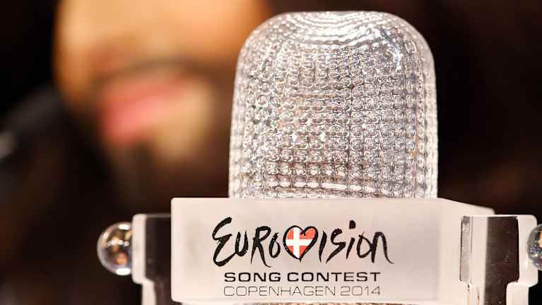 Euroviisujen lasinen voittopokaali joka on mikrofonin muotoinen, taustalla Conchita Wurst.