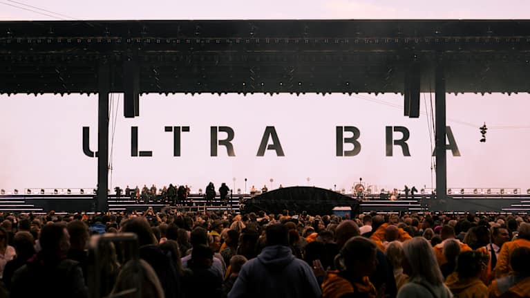 Ultra Bran konsertin tunnelmaa Olympiastadionilta. Kuvassa on suuri lava, jossa yhtye soittaa. Yleisössä paljon keltaisiin sadetakkeihin pukeutuneita konserttivieraita.