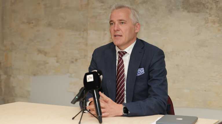 Opetusministeri Anders Adlercreutz istuu pöydän takana mikrofonin edessä.