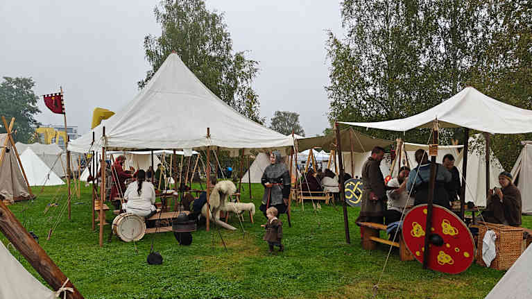 Perinteisiä kangastelttoja, joissa on puutuennat, ihmisiä perinnevaatteissa.
