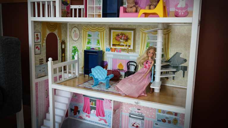 Kuvassa kolmikerroksinen nukkekoti. Keskimmäisessä kerroksessa istuu vaaleanpunaiseen pukeutunut Barbie-nukke.