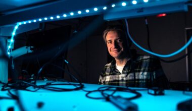 Robert Fickler sits in a photonics laboratory lit by blue light.