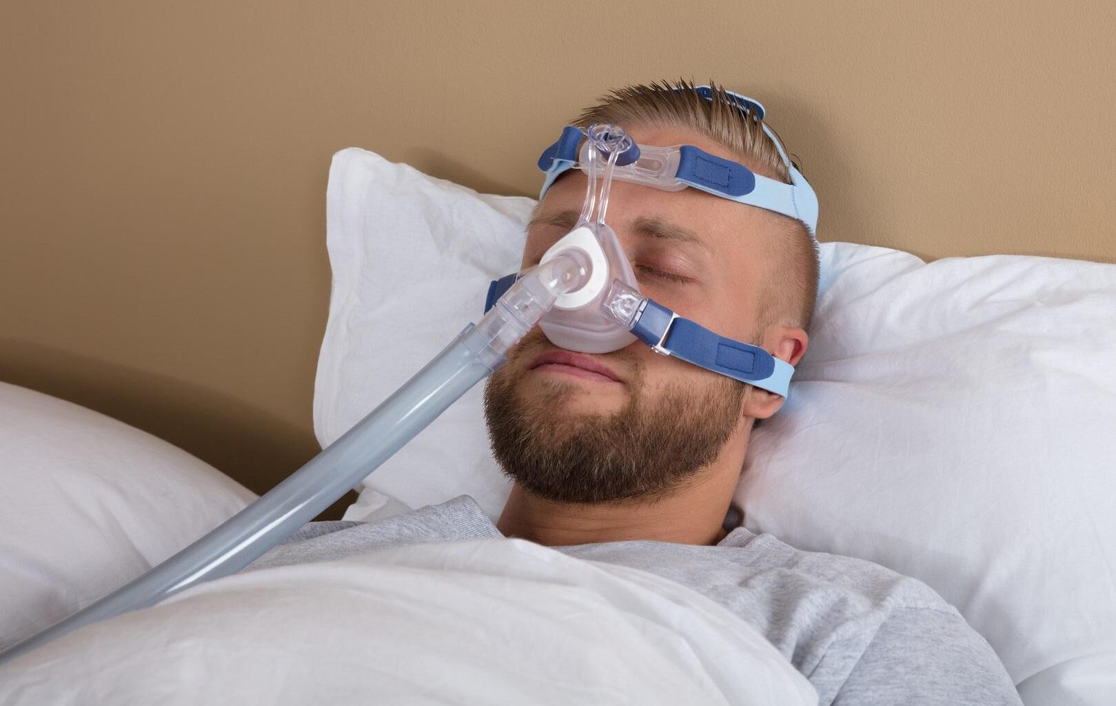Mies nukkuu selällään CPAP-laitteen nenämaski kasvoillaan.