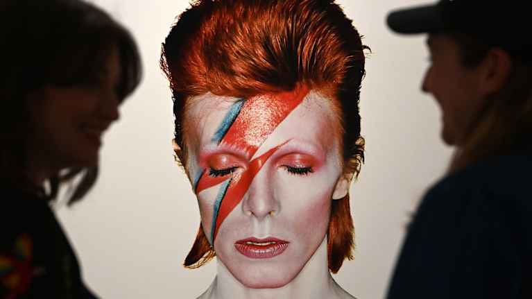 David Bowien Aladdin Sane -hahmon lähikuva seinällä, reunoilla sitä katsovat mustat siluettihahmot.