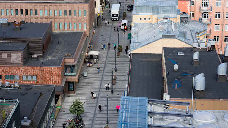 Näkymä Oulun keskustaan yläviistosta, kauppakeskus Valkean katolta, ihmisiä kävelemässä kadulla, horisontissa Rommakonselkä ja Pikisaari.