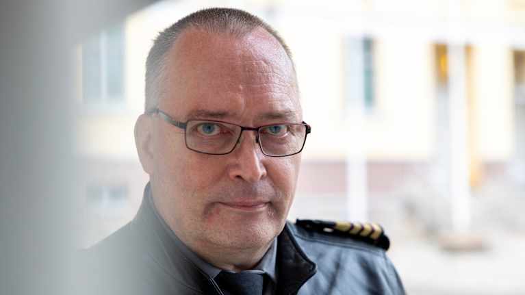 Nahkatakkinen mies seisoo rakennuksen vierustalla.