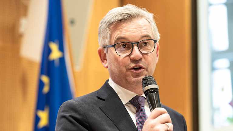 Mies pitää puhetta mikrofoni kädessään Euroopan unionin lippu taustallaan.