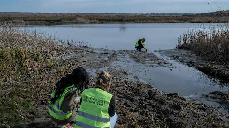Ihmisiä huomiliiveissä joen rannalla näytteitä ottamassa.