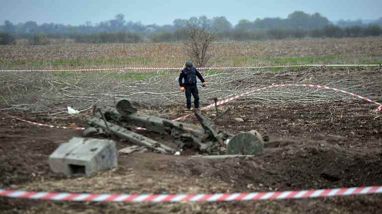 Nauhoin suljettu kuoppa jossa on aseromua ja kypäräpäinen mies tarkastamassa tilannetta.