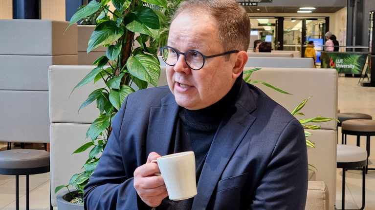 Rehtori Juha-Matti Saksa rentoutumassa kahvikupin ääressä modernissa kahvilaympäristössä.