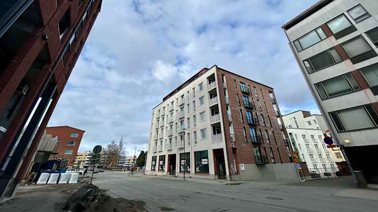 Kuvassa kerrostalo ja edessä tyhjää tietä.