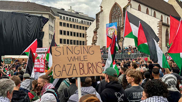 Ihmiset osoittavat mieltään, heiluttavat palestiinan lippuja ja kylttejä, joista lähimmässä lukee: Singing while Gaza burns.