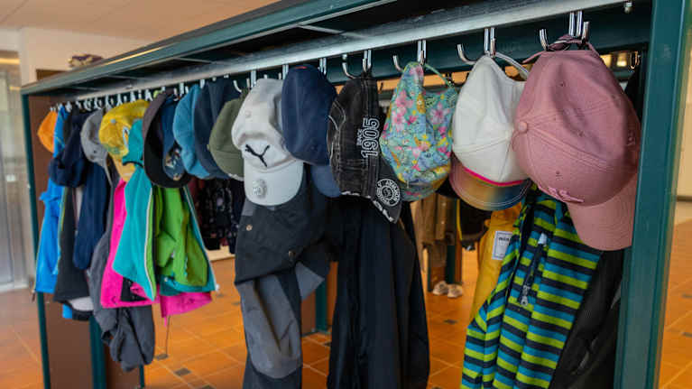 Naulakko, jossa roikuu värikkäitä lasten lippalakkeja ja takkeja.