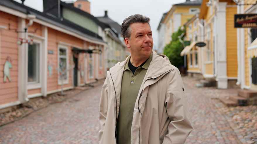 Mies seisoo kadulla, jonka varrella on puutaloja.