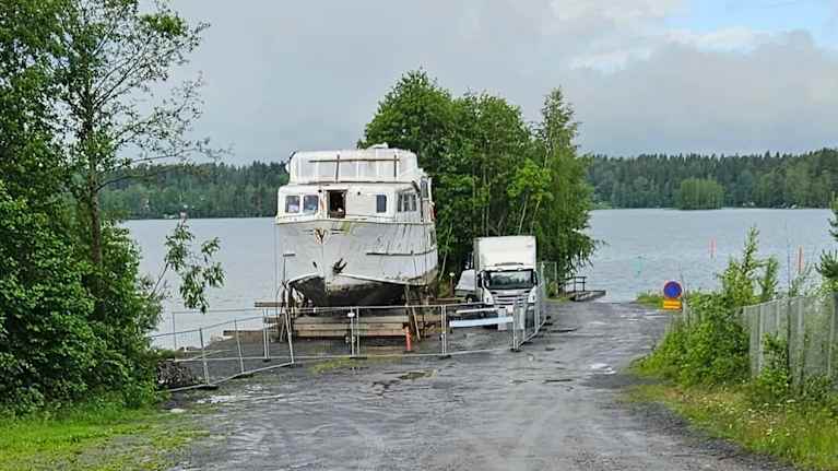 Sisävesialus M/S Tampere telakalla Valkeakoskella, aidalla ympäröitynä. Taustalla järvenrantaa.