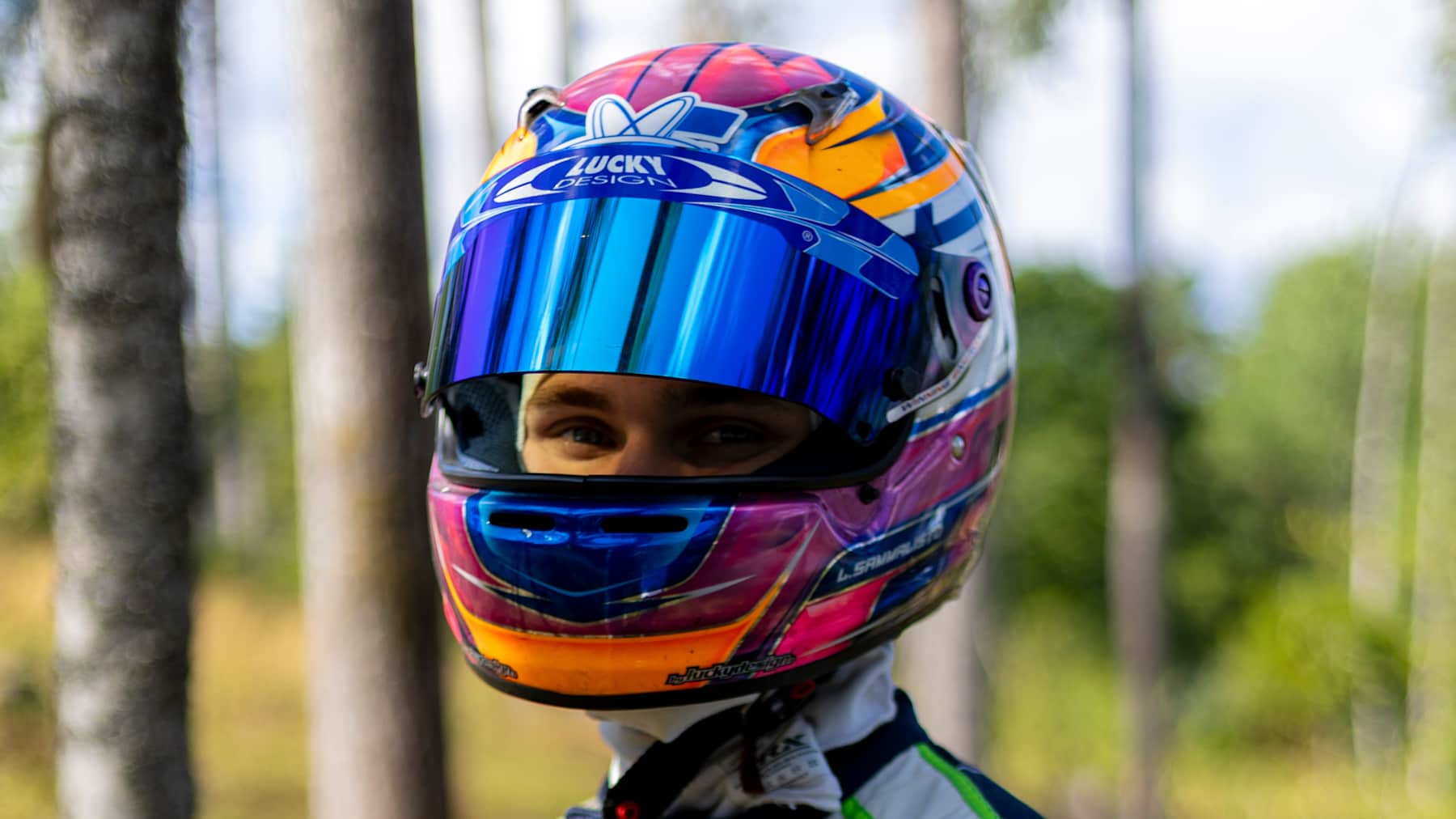 Formula 4 -kuljettaja Luka Sammalisto poseeraa kisavarustuksessa puiden seassa.