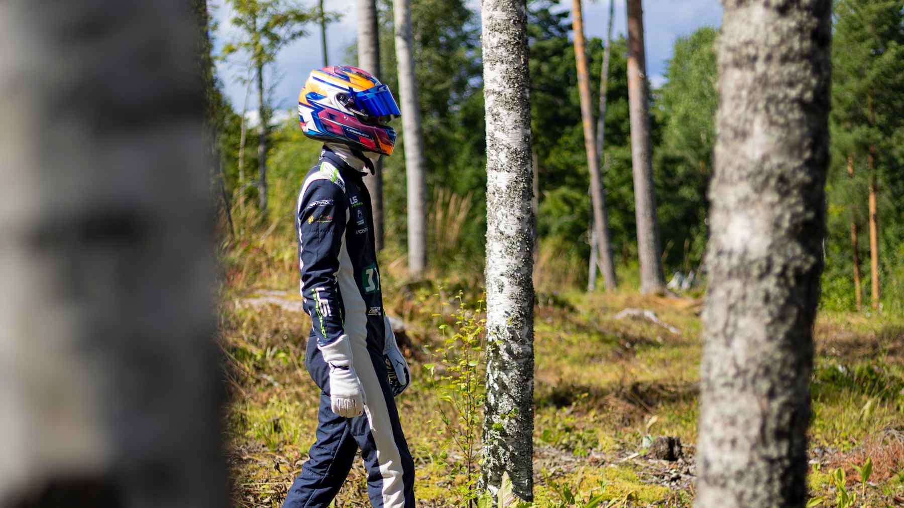 Formula 4 -kuljettaja Luka Sammalisto kävelee kisavarustuksessa puiden seassa.