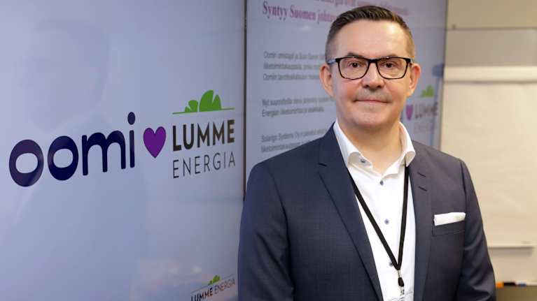 Suur-Savon Sähkön toimitusjohtaja Mikael Venäläinen seisoo näytön edessä. Näytöllä on Oomin ja Lumme Energian logot.