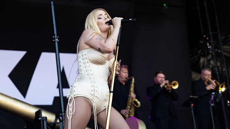 Erika Vikman lavalla kultaisessa korsettiasussa ja valkoisissa, pitkissä nahkasaappaissa laulamassa intohimoisesti.