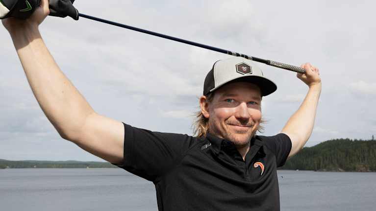 Sami Vatanen katsoo kameraan kannatellessaan golfmailaa päänsä päällä.