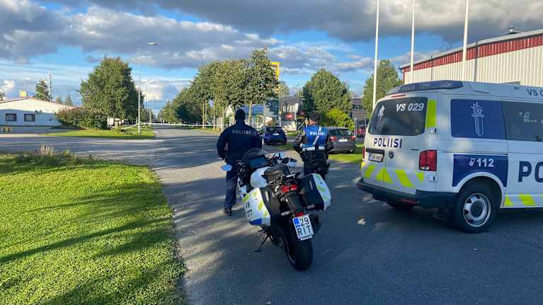 Kaksi poliisia, poliisin moottoripyörä ja poliisiauto keskellä katua.