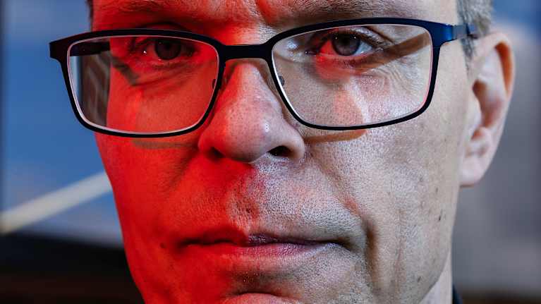 Professori Samuel Kaski poseeraa kameralle Otaniemessä. Kasken kasvoille osuu punainen valo.