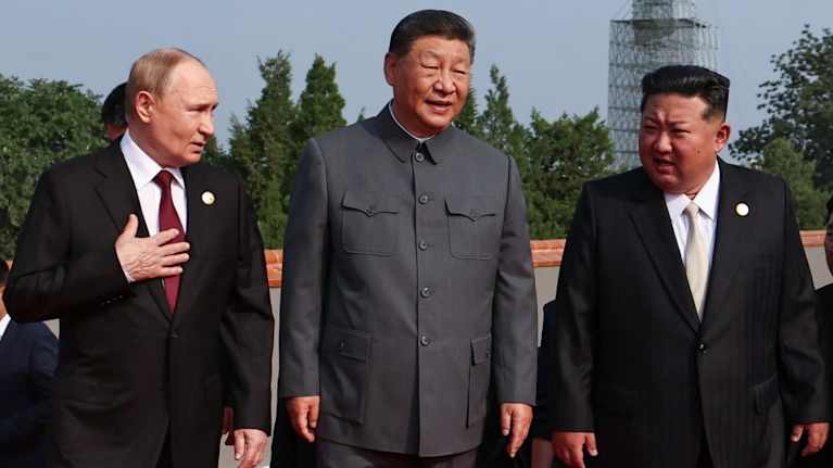 Vladimir Putin, Xi Jinping ja Kim Jong-un kävelevät punaisella matolla vierekkäin.