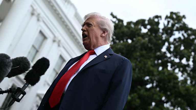 Donald Trump puhuu edessään mikrofonien rykelmä. Taustalla näkyy Valkoisen talon julkisivu.