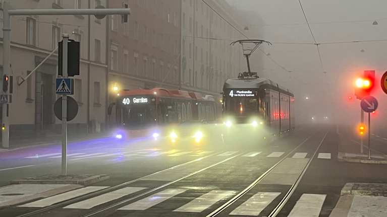 Raitiovaunu ja linja-auto liikenteessä sumuisena aamuna Helsingissä.
