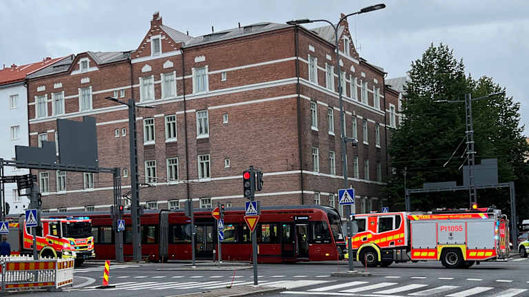 Kadun keskellä palokunnan autoja, poliisiajoneuvoja ja raitiotievaunu.