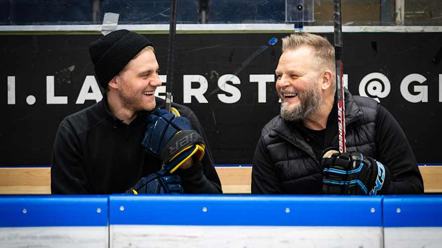Wiljami Myllylä ja Marko Jantunen istuvat jääkiekkokaukalon vaihtoaitiossa. Miehet katsovat toisiaan ja hymyilevät.