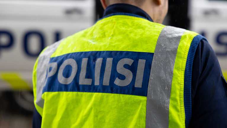 Poliisi seisoo huomioliivissä poliisiauton edustalla.