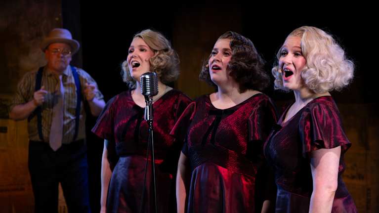 Kolme naisnäyttelijää esittämässä Valtosen siskoksia näytelmään Harmony sisters. Taustalla miesnäyttelijä esittämässä Yleisradion edustajaa.
