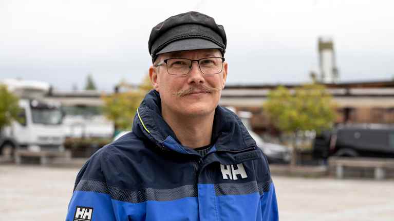 Mies seisoo ulkona yllään sininen takki ja musta lippalakki. 