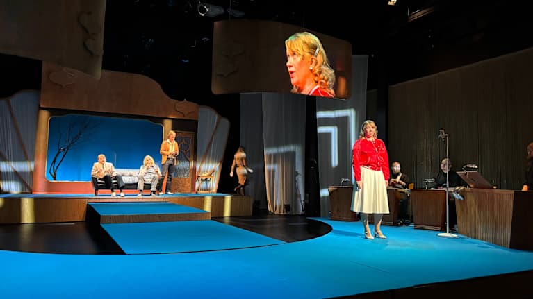 Armi Aavikkoa näyttelevä Milla Kuikka seisoo koelaulutilaisuudessa teatterinnäyttämöllä, josta on lavastettu studio.