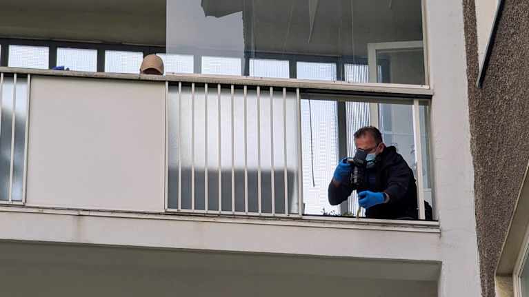 Hengityssuojaimeen pukeutunut poliisi tutkii parvekkeen reunaa, josta puuttuu suojalevy. 