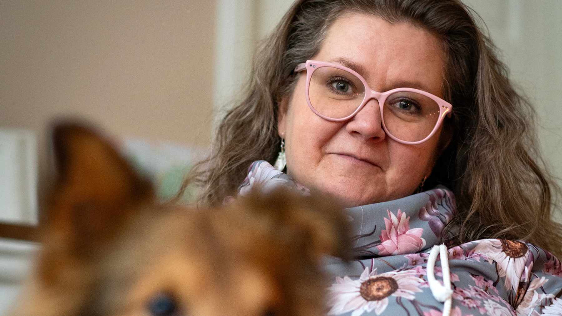 Essi Sivula istuu sohvalla. Hänen edessään on collie-rotuinen koira epäterävänä.